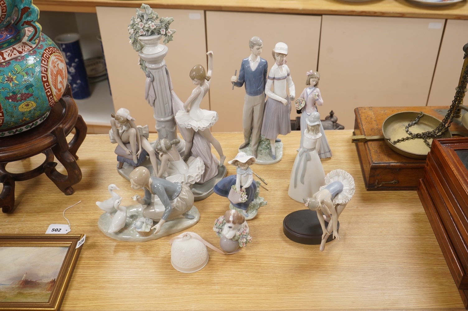 A large Lladro figure group of three ballet dancers by a tall floral column and eight other Lladro figures including a model of a bell. Tallest figure group 45cm high. Condition - golfer group, golf clubs broken.